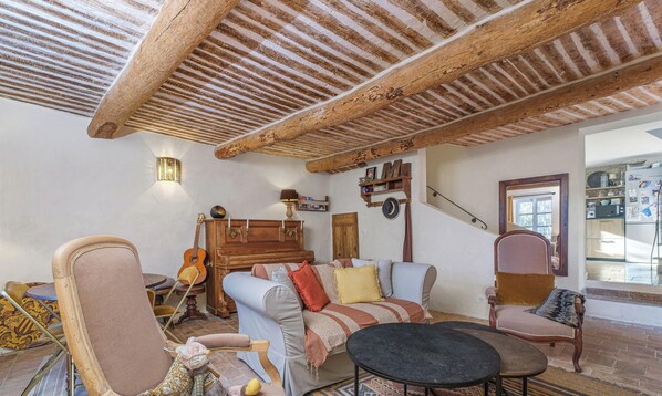 Un interior rústic amb bigues de fusta al descobert, un piano, una guitarra i una zona de menjador amb cadires i taula.