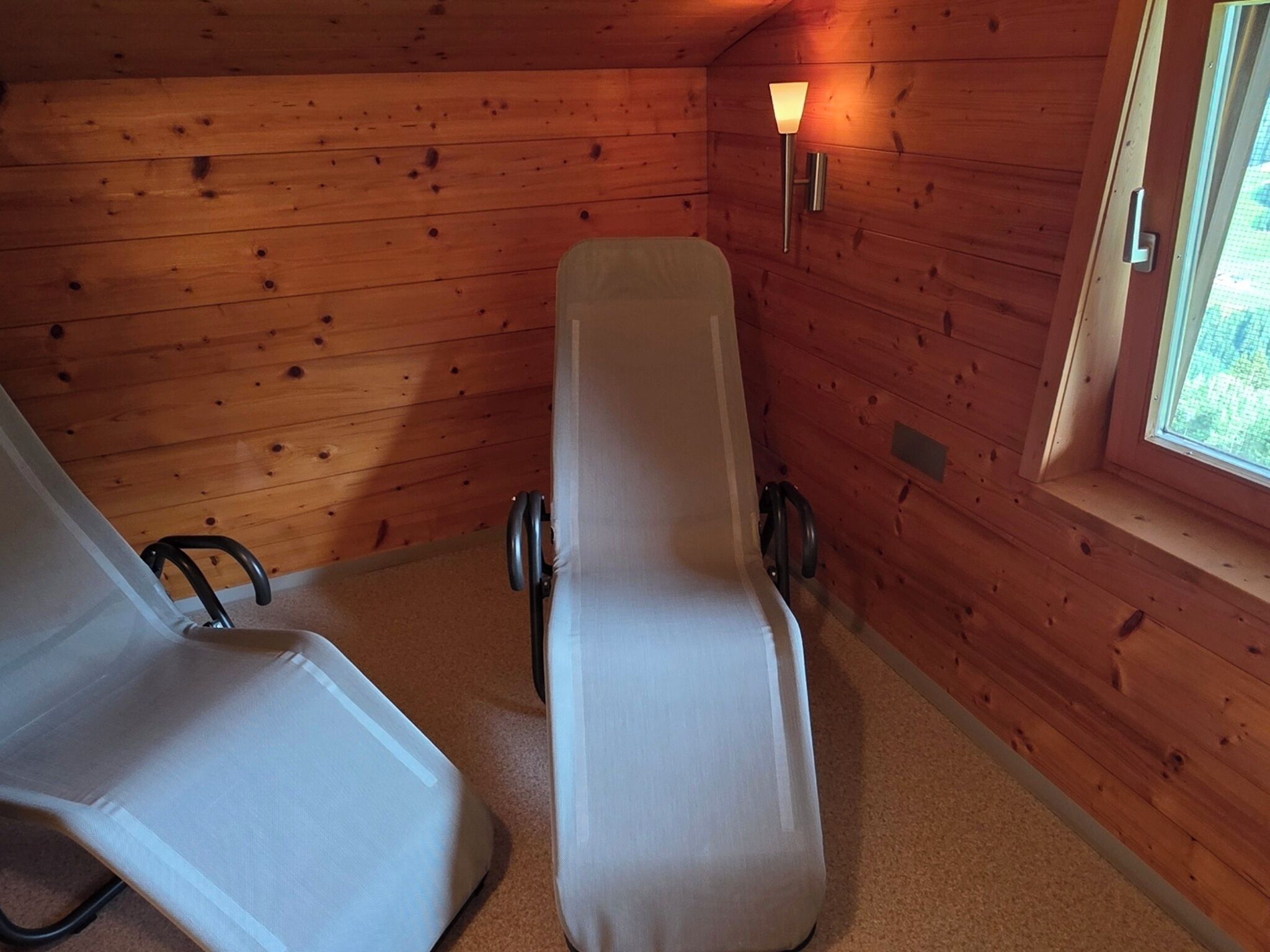 A wooden cabin room with a single bed, a chair, and a window.