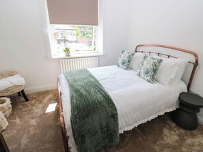 Un dormitorio con una cama, ventana, radiador, silla y mesita de noche.