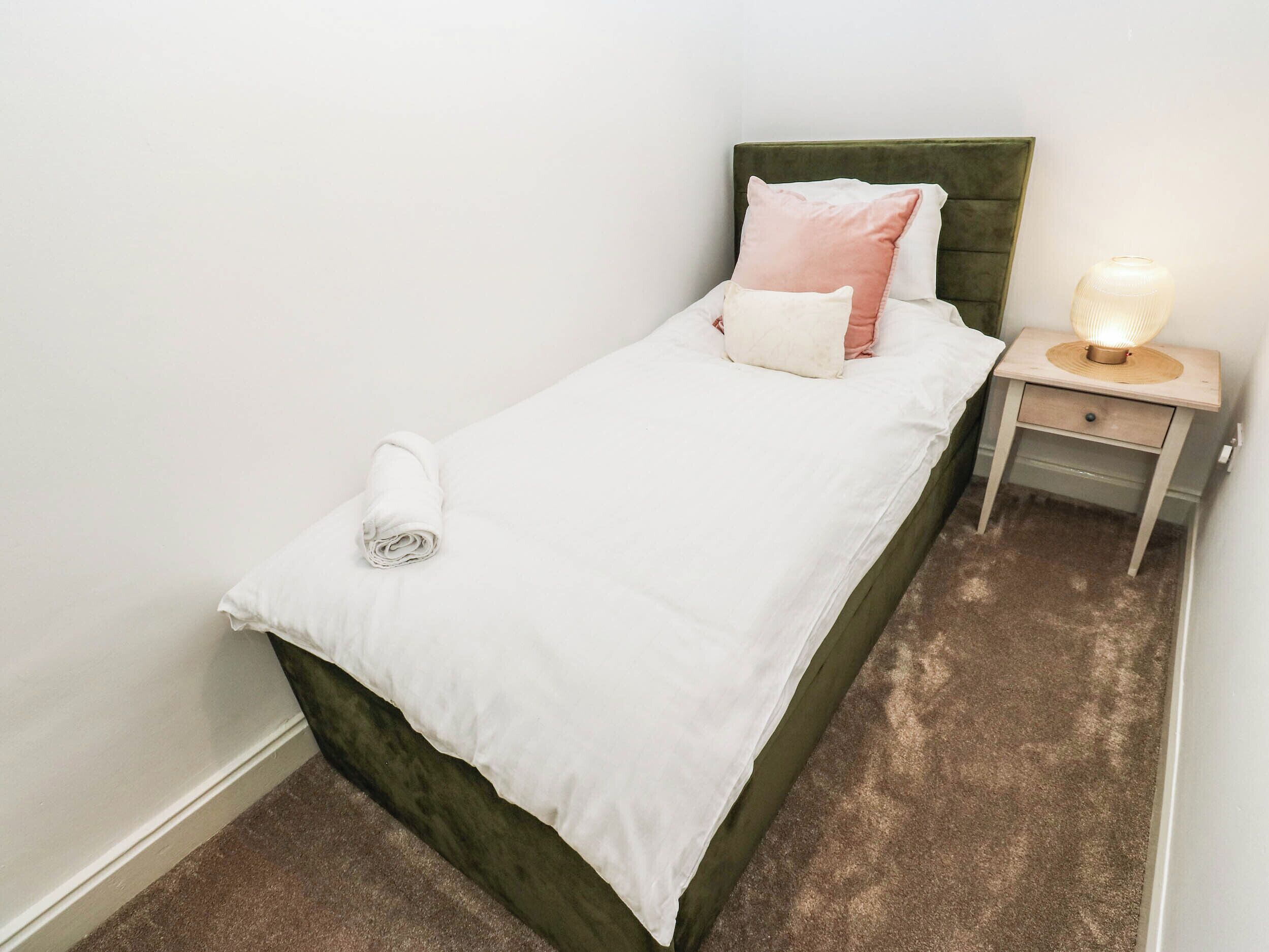 Uma cama de solteiro com cabeceira verde, roupa de cama branca e uma luminária de cabeceira.
