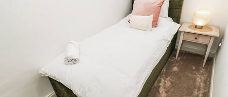 A single bed with a green headboard, white bedding, and a bedside lamp.
