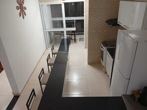A kitchen with a refrigerator, stove, and dining area with chairs and a table. - Beach apartment (Ubatuba)