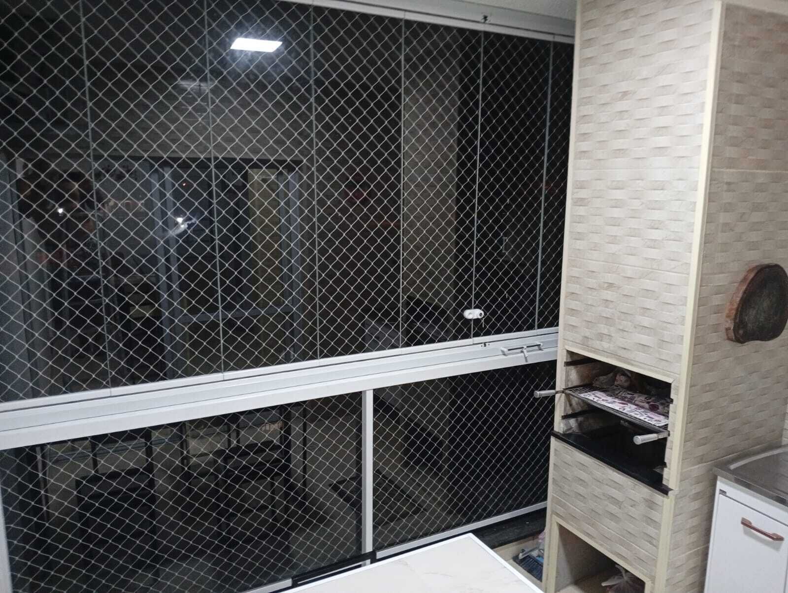 A room with a large window covered by a metal mesh screen, a white cabinet with drawers, and a tiled wall.