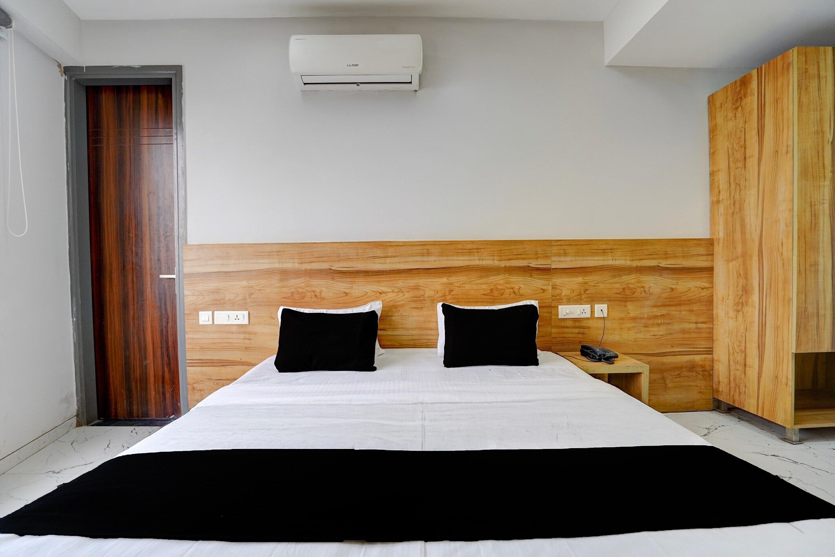 Et hotelværelse med en seng, et træpanelt sengegærde, et natbord med en telefon og en aircondition-enhed.
