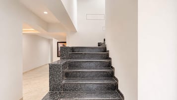 A modern interior with a staircase leading to a higher floor, white walls, and a marble floor.