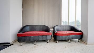 Two black leather armchairs with red cushions in a room with a marble floor and a large window.