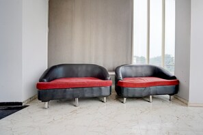 Dos sillones de cuero negro con cojines rojos en una habitación con suelo de mármol y un ventanal grande.