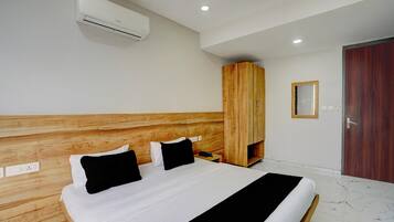 Habitación de hotel con cabecera de madera, cama con ropa de cama blanca y negra, unidad de aire acondicionado, armario de madera y puerta con espejo.