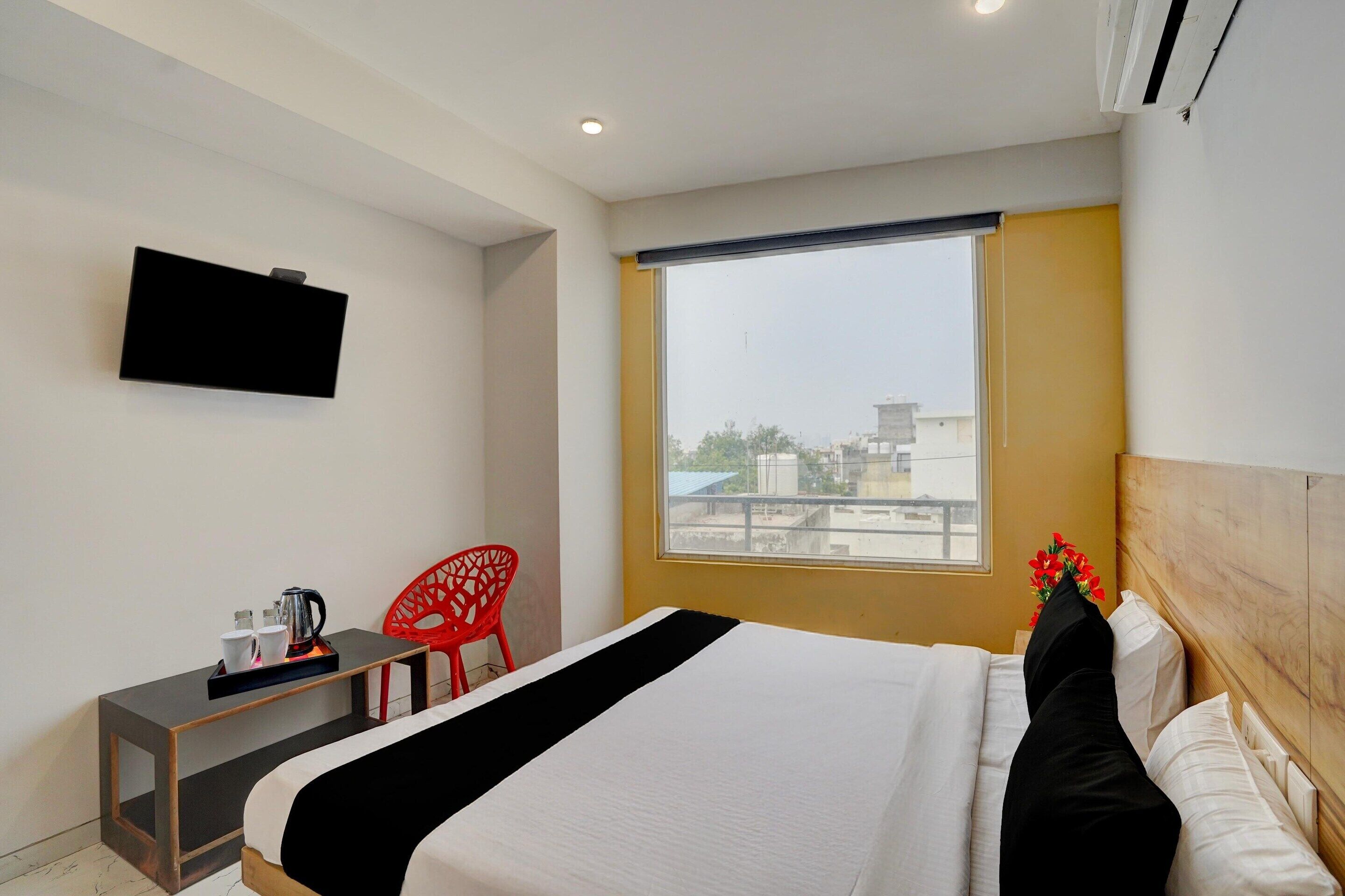 A hotel room with a bed, a desk, a chair, a television, and a window with a view of buildings.