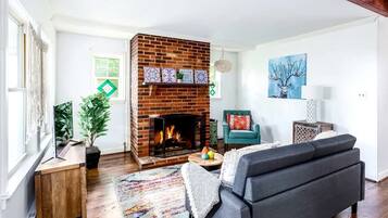 A living room with a brick fireplace, a sofa, a chair, and a table with a lamp.