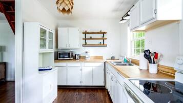 A modern kitchen with white cabinetry, a wooden countertop, a built-in microwave, and a hanging light fixture.