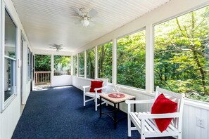 Une véranda avec une table et des chaises, de grandes fenêtres et un ventilateur de plafond.