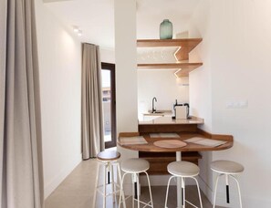 Eine kleine Küche mit einer Holzausziehtafel, einem Spülbecken und einer Vase auf einem Regal. Vier Stühle stehen an der Theke.