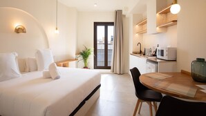 Et hotelværelse med seng, spisebord med stole, et tekøkken og udsigt gennem en dør.