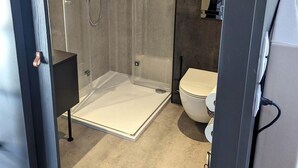 Een moderne badkamer met een douchecabine van glas, een wit toilet en een donkere kast.