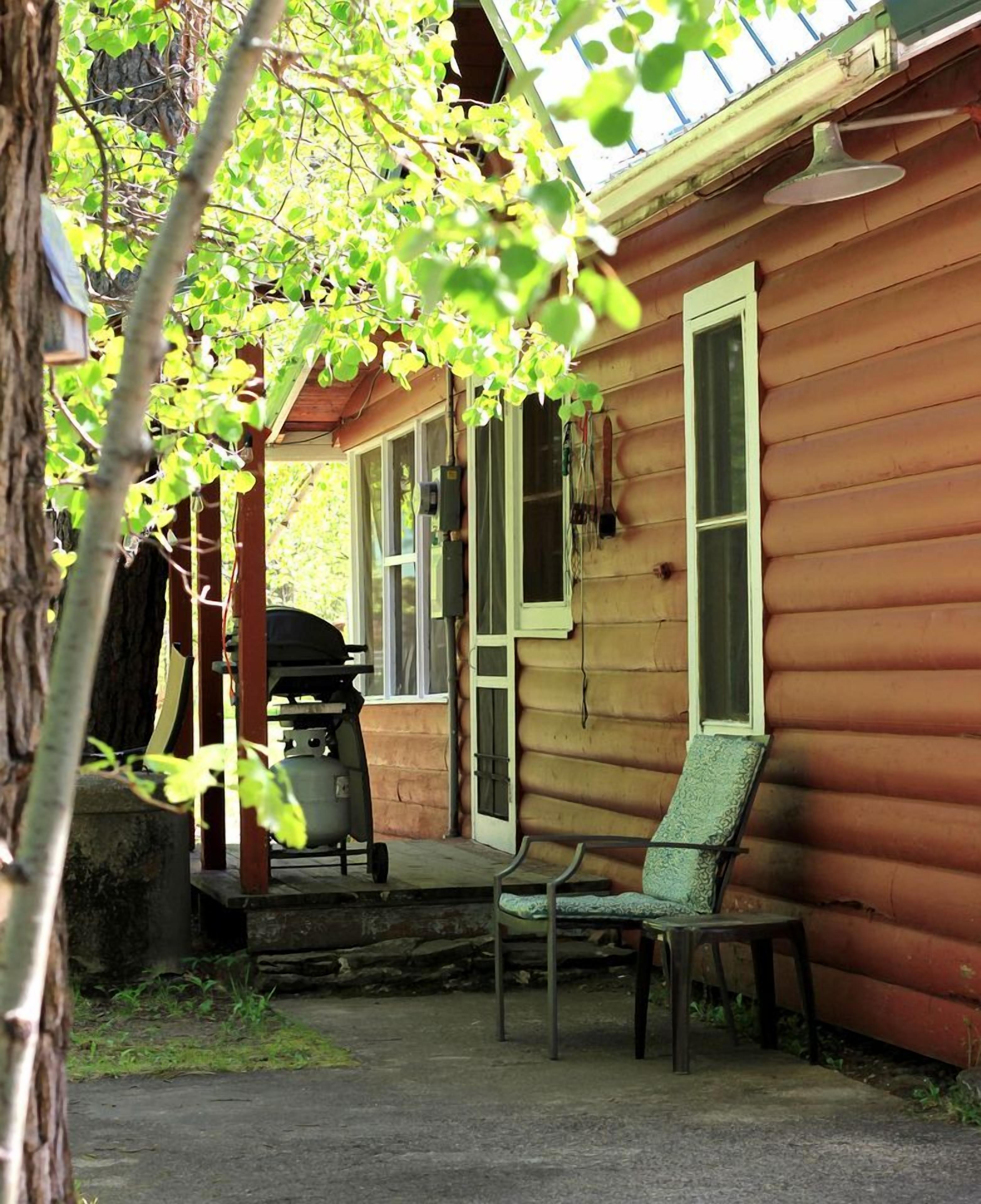 A wooden cabin with a porch, a grill, and a chair.