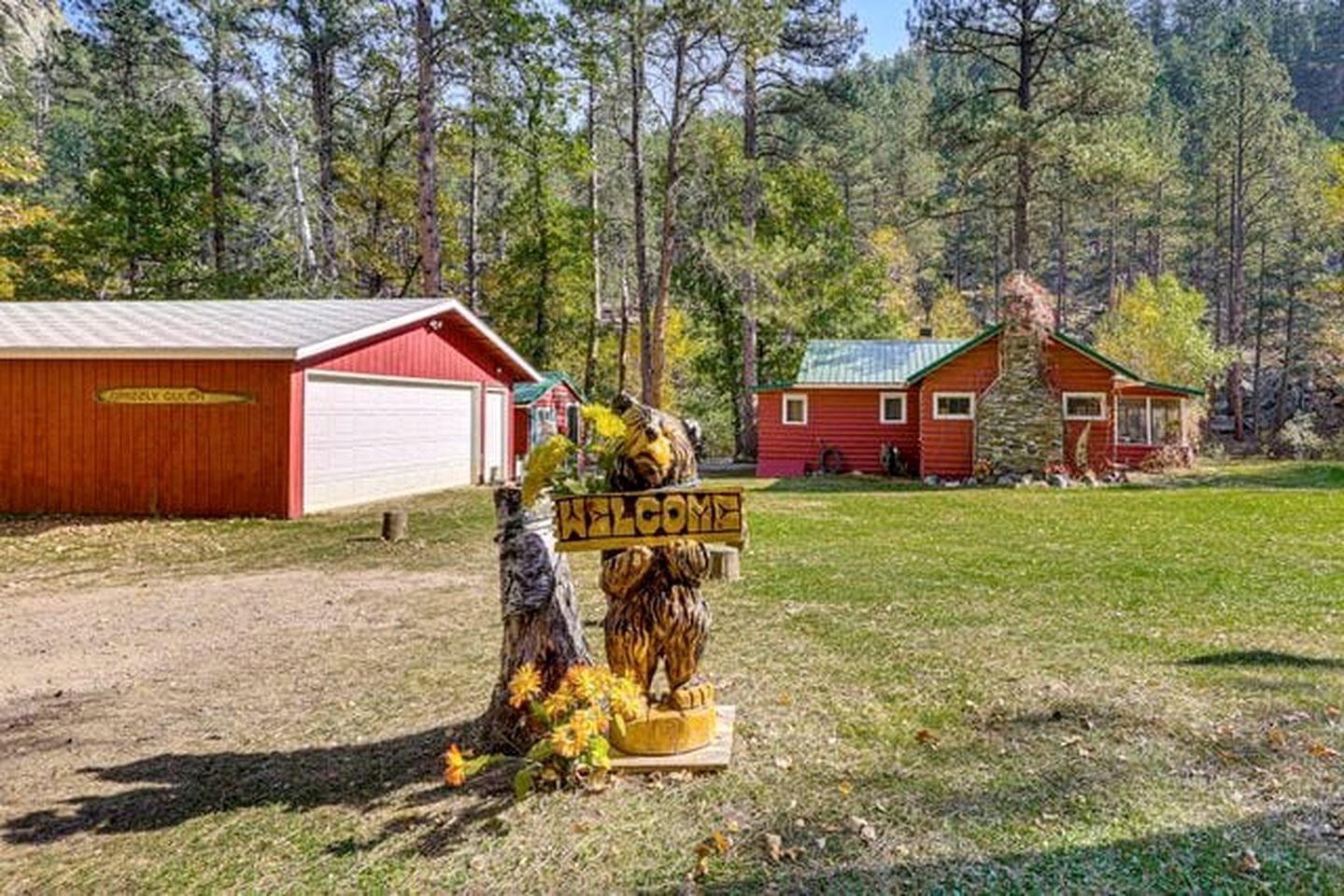 A rustic cabin with a red exterior, a garage, and a welcome sign with a bear figure.