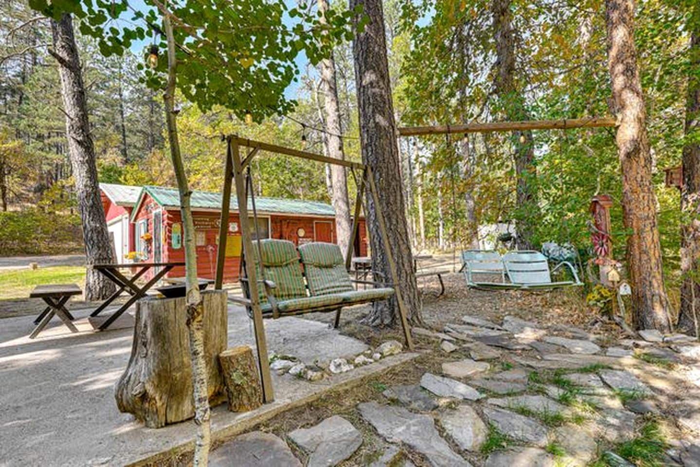 A rustic outdoor seating area with a swing, picnic table, and a small cabin-like structure.