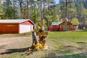 Uma cabana rústica com fachada vermelha, uma garagem e uma placa de boas-vindas com a figura de um urso.