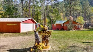 Una baita rustica con facciata rossa, un garage e un cartello di benvenuto con una figura di orso.