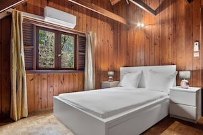 A wooden-paneled room with a bed, bedside tables, and an air conditioning unit.