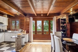 A modern kitchen with granite countertops, a dining area with a table and chairs, and large windows with a view of greenery.