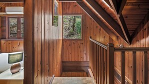 Een houten interieur met een trap, een raam met uitzicht op groen, en een witte airconditioning.