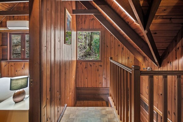 A wooden interior with a staircase, a window with a view of greenery, and a white air conditioning unit.