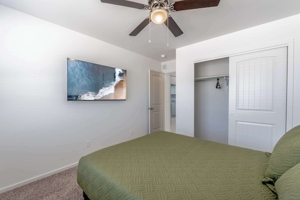 A bedroom with a bed, a ceiling fan, a wall-mounted TV, and a closet.