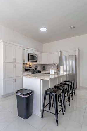A modern kitchen with white cabinets, stainless steel appliances, a granite countertop, and black bar stools.