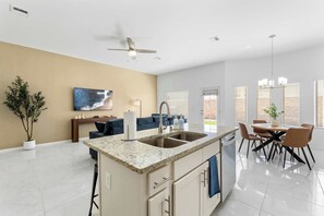 A modern kitchen with a central island, a dining area with a table and chairs, a ceiling fan, and a large window with blinds. - Desert Modern 3BR 2BA Home  King Bed  Smart TVs (El Paso)