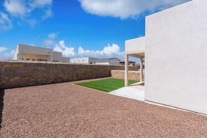A modern outdoor area with a stone wall, gravel ground, and a grassy patch. - Desert Modern 3BR 2BA Home  King Bed  Smart TVs (El Paso)