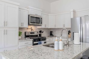 Una cocina moderna con armarios blancos, un refrigerador de acero inoxidable, un microondas, una estufa a gas y un lavamanos con grifo.
