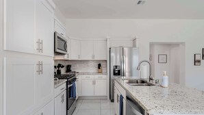 A modern kitchen with white cabinetry, stainless steel appliances, a granite countertop, and a built-in dishwasher.