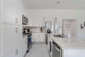 A modern kitchen with white cabinetry, stainless steel appliances, a granite countertop, and a built-in dishwasher. - Desert Modern 3BR 2BA Home  King Bed  Smart TVs (El Paso)