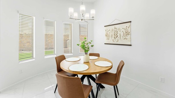 A dining room with a round table, four chairs, a chandelier, and a wall-mounted artwork.