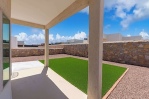 A modern outdoor patio with artificial grass, stone walls, and a clear view of the sky.