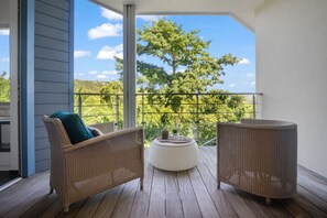 Ein Balkon mit Korbmöbeln, einem weißen runden Tisch und Blick auf Bäume und Himmel.