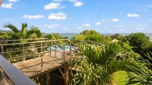 A wooden deck with a pool, surrounded by tropical plants, overlooking a body of water. - Villa El Desert, right on the water (Sainte-Luce)