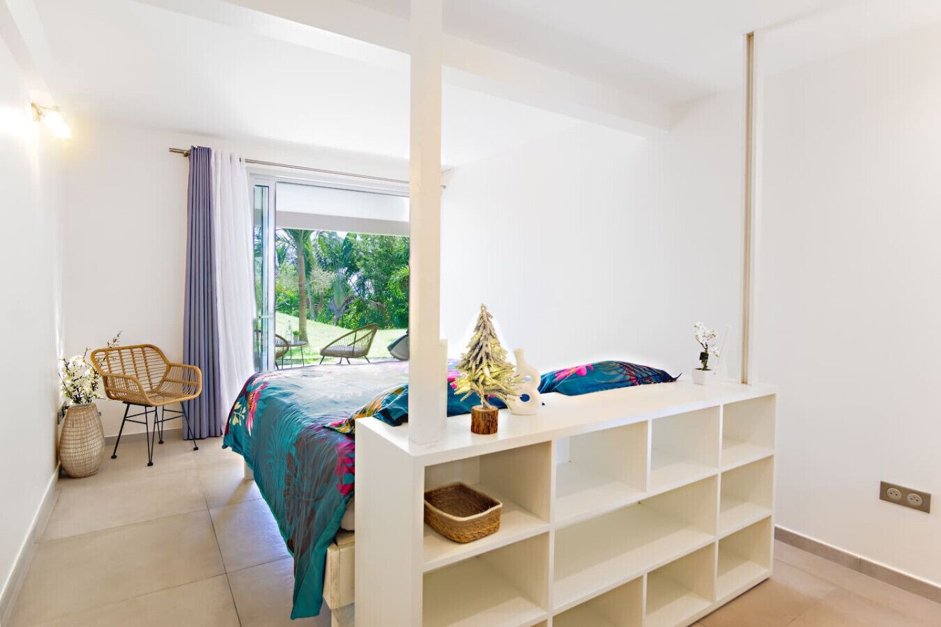 A bedroom with a bed, a white console table, a chair, and a view of the outdoors.