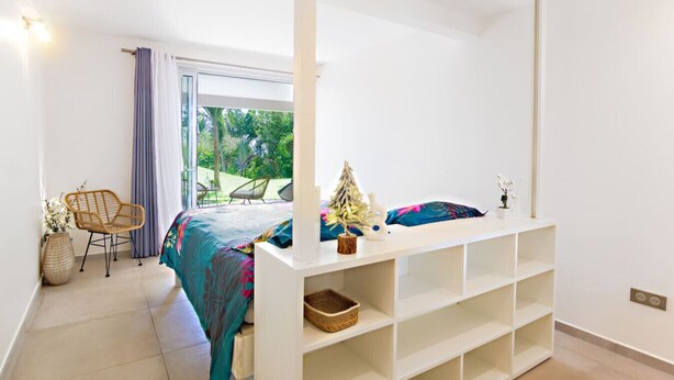 A bedroom with a bed, a white console table, a chair, and a view of the outdoors. - Villa El Desert, right on the water (Sainte-Luce)