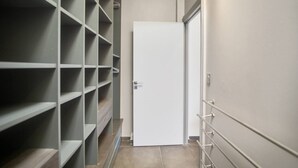 A narrow hallway with a white door at the end, flanked by metal shelving units with no visible contents. - Villa El Desert, right on the water (Sainte-Luce)