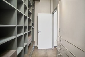 Ein schmaler Flur mit einer weißen Tür am Ende, begleitet von Metallregalen, die leer sind.