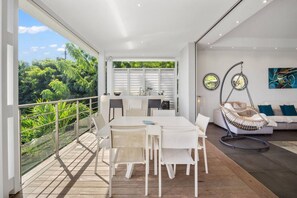 Een modern interieur met een eethoek, een hangstoel en uitzicht op weelderige begroeiing.
