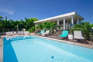 Ein Schwimmbecken mit Liegestühlen und einer überdachten Liegefläche.