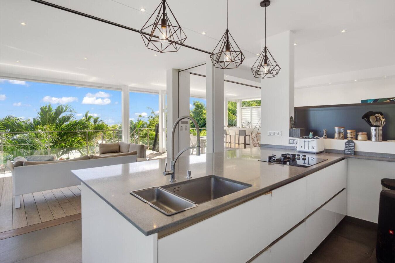 Une cuisine moderne dotée d’un grand îlot central, d’appareils électroménagers en acier inoxydable et de luminaires suspendus.