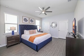 Ein Schlafzimmer mit Bett, Nachttischen, Deckenventilator, Fernseher und Kunstwerken an den Wänden.