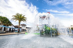 A fountain with water jets, palm trees, and a building with a sign. - Bengal Court Reserve (Kissimmee)