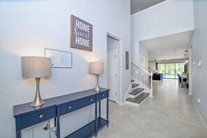 A modern interior with a console table, two lamps, a staircase, and a view into a dining area. - Bengal Court Reserve (Kissimmee)