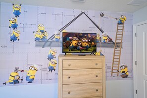 A room with a television on a wooden cabinet, a ladder, and minion-themed decorations on the wall. - Bengal Court Reserve (Kissimmee)